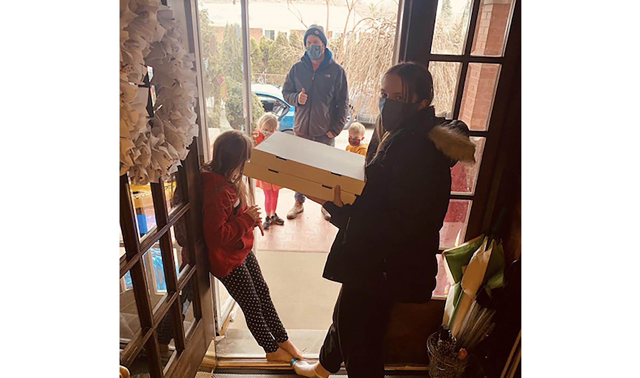 Two young people at their front door receiving pizza delivery from YU staff